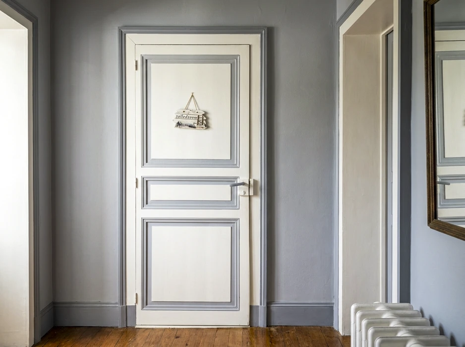 Couloir intérieur élégant avec une porte à panneaux moulurés blanc et gris perle, ornée d'un panneau décoratif suspendu