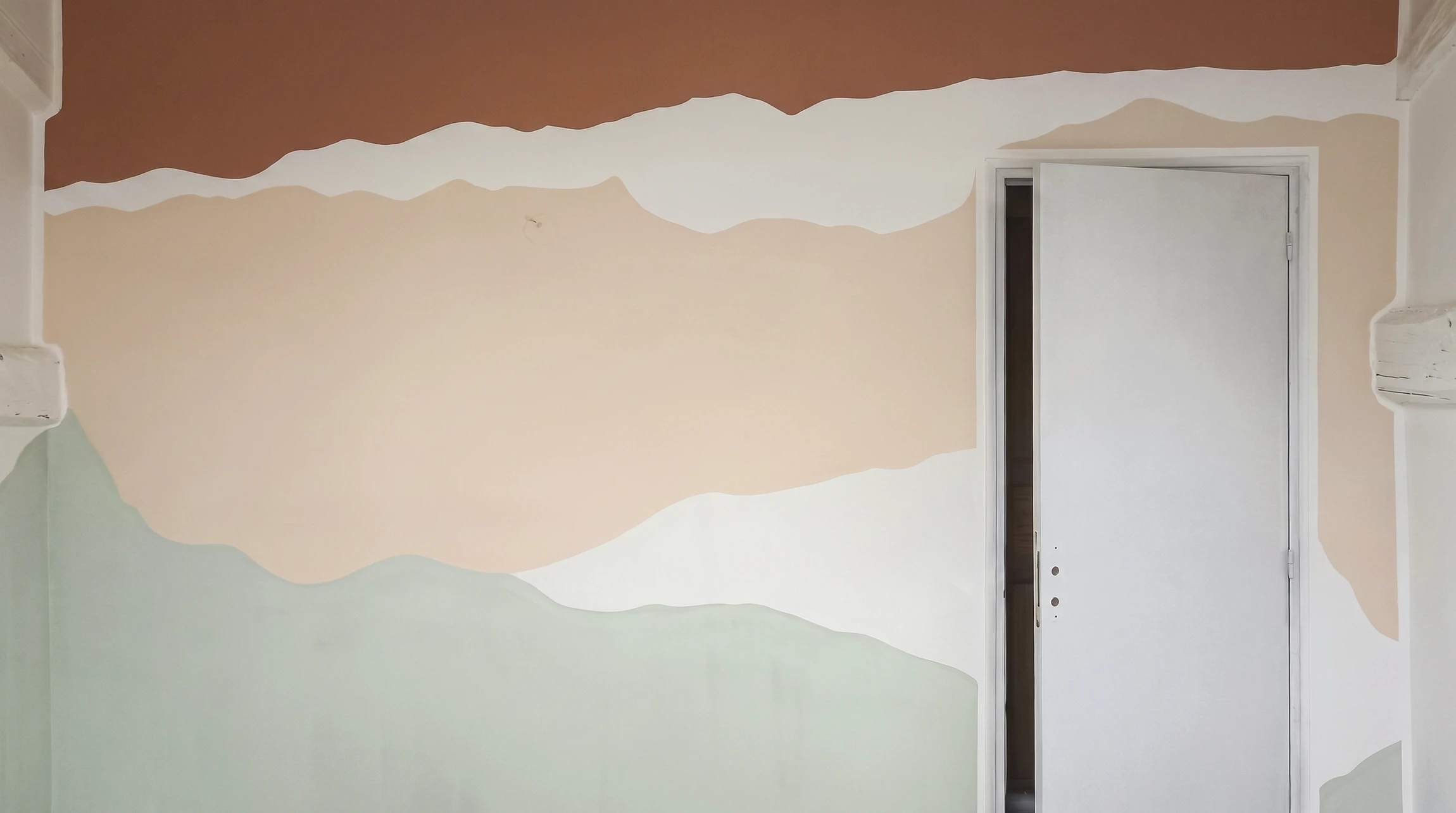 Mur intérieur peint avec un motif paysager abstrait en aplats ondulés superposés : terracotta en haut, pêche au centre, blanc cassé et vert sauge en bas