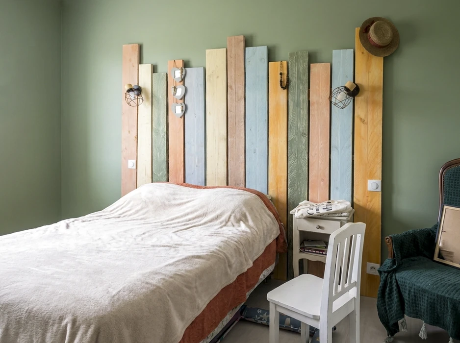 Chambre à coucher avec tête de lit DIY composée de planches de bois verticales peintes en couleurs pastel (bleu, vert, beige, orange, jaune)