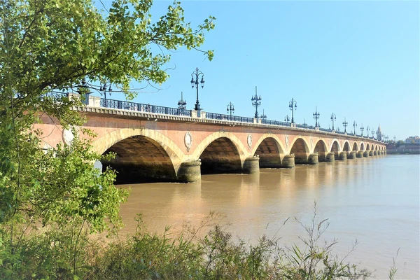 Une photographie réaliste et professionnelle de la ville de Bordeaux montrant ses monuments caractéristiques et son architecture emblématique : la Cité du Vin avec sa structure moderne distinctive, les façades classiques du centre-ville, la Garonne en premier plan ou arrière-plan, l'atmosphère urbaine vibrante du centre historique avec ses bâtiments en pierre de taille aux couleurs chaudes, et idéalement une vue qui capture l'essence touristique et monumentale de Bordeaux comme métropole régionale du Sud-Ouest français. Image sans texte ni logo visible.